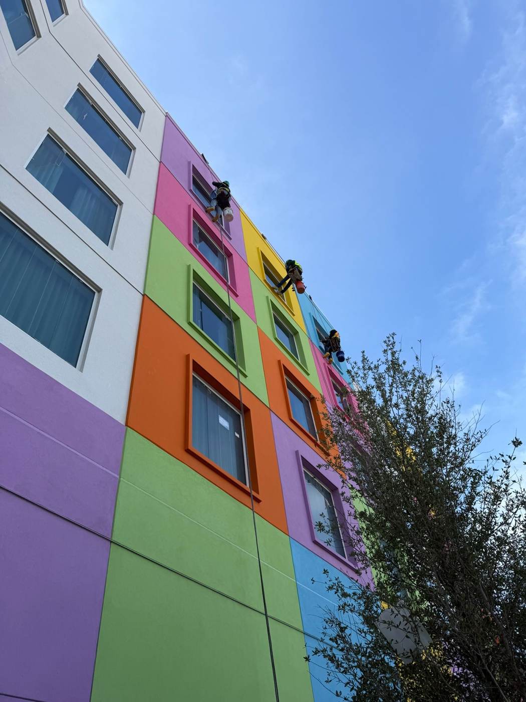 Three rope-access techs cleaning windows on a colorful Universal hotel